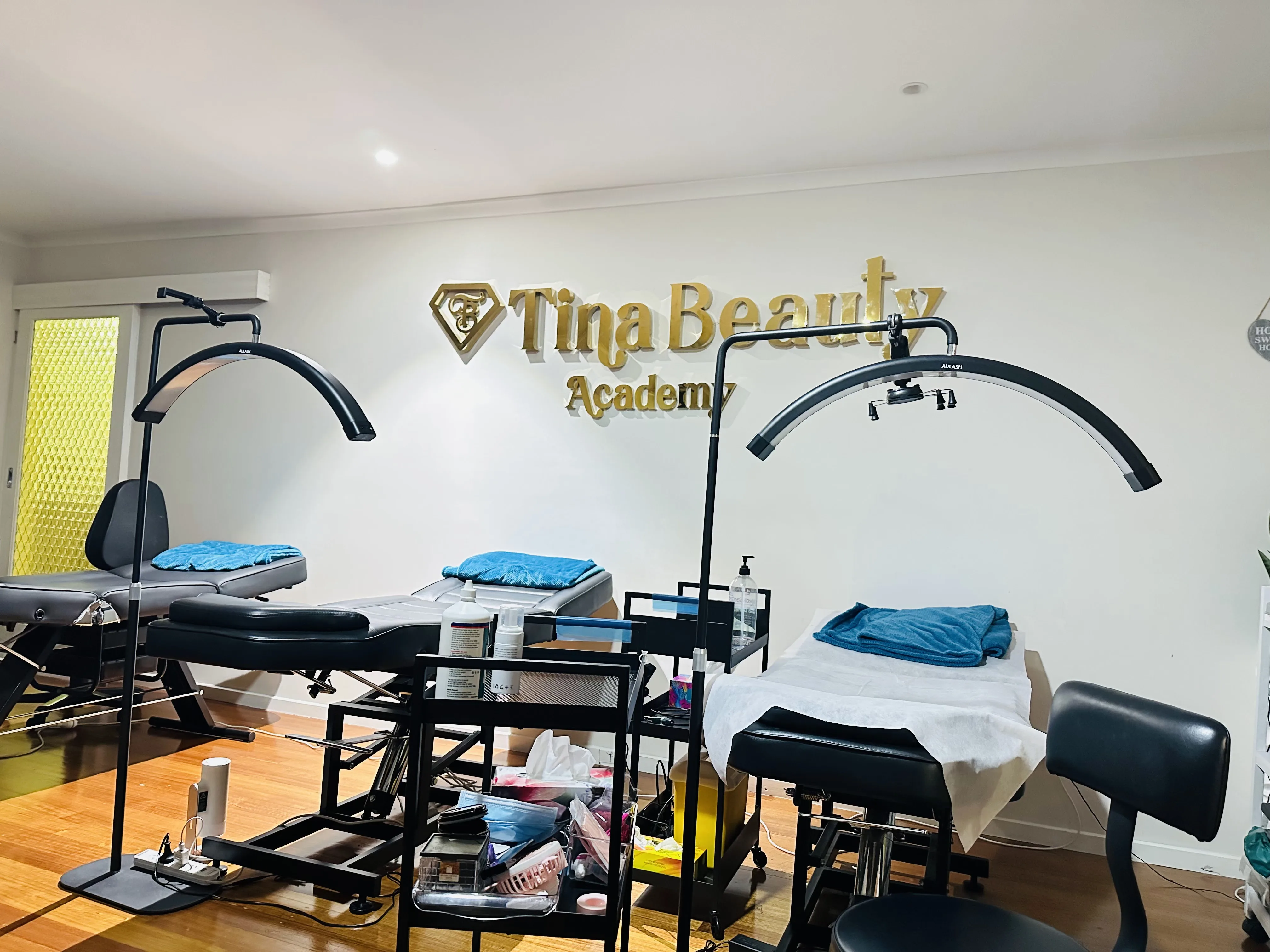 Tina Beauty Academy treatment room interior — branded gold wall sign, arc lamps and honey timber floor